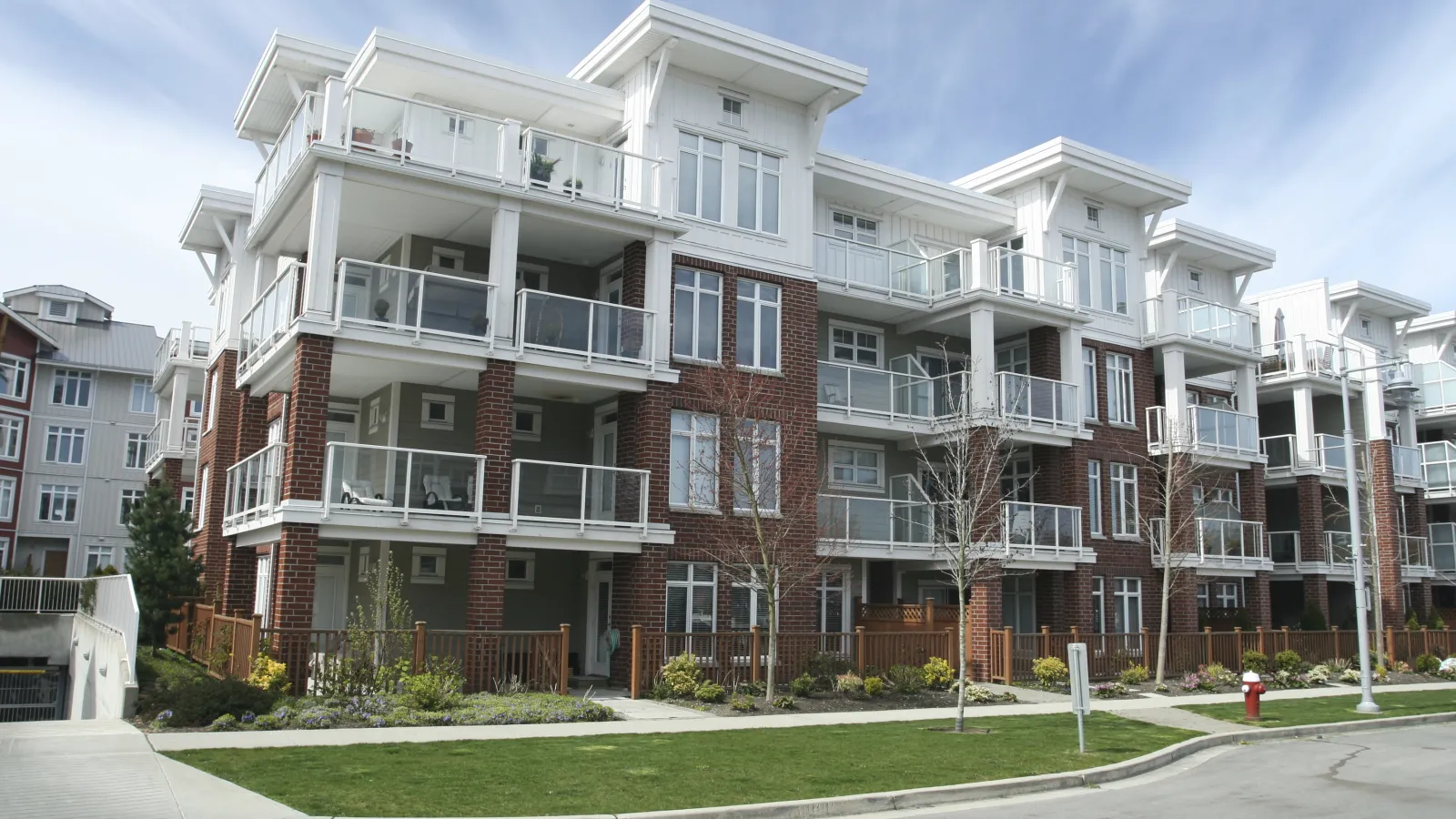 Modern multi-story apartment building with balconies, brick and white exterior under a blue sky.