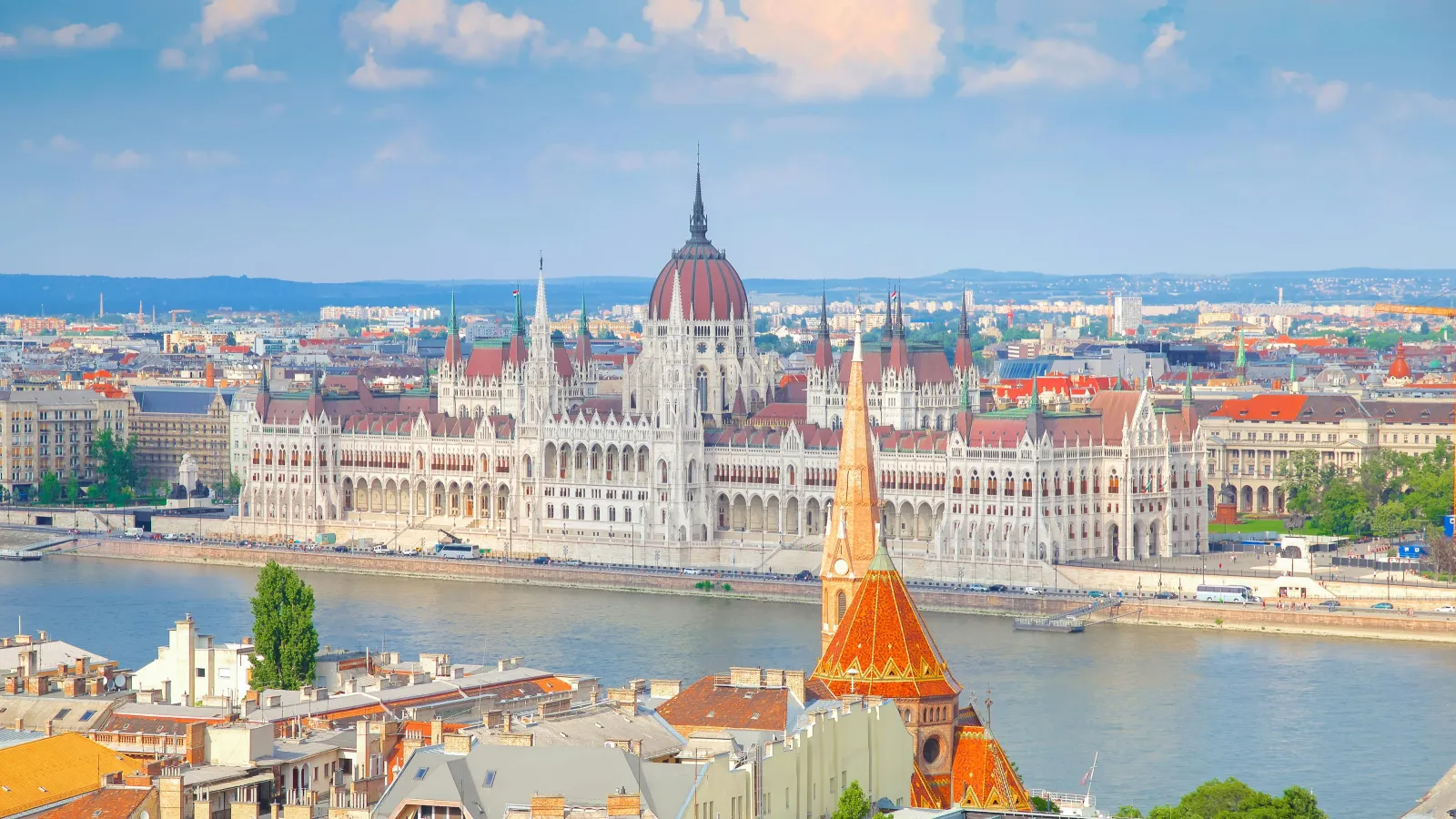 View of the Hungarian Parliament and Danube River in Budapest with clear skies and cityscape in the background.
