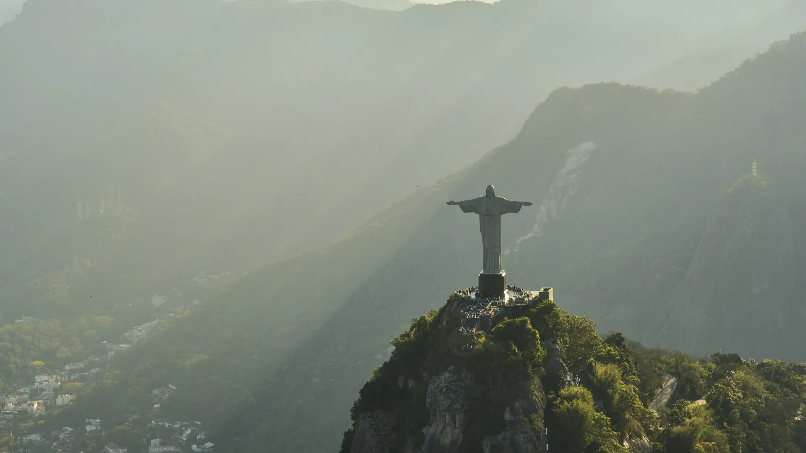 Statue of Christ the Redeemer atop a mountain overlooking Rio de Janeiro with misty mountains in the background.