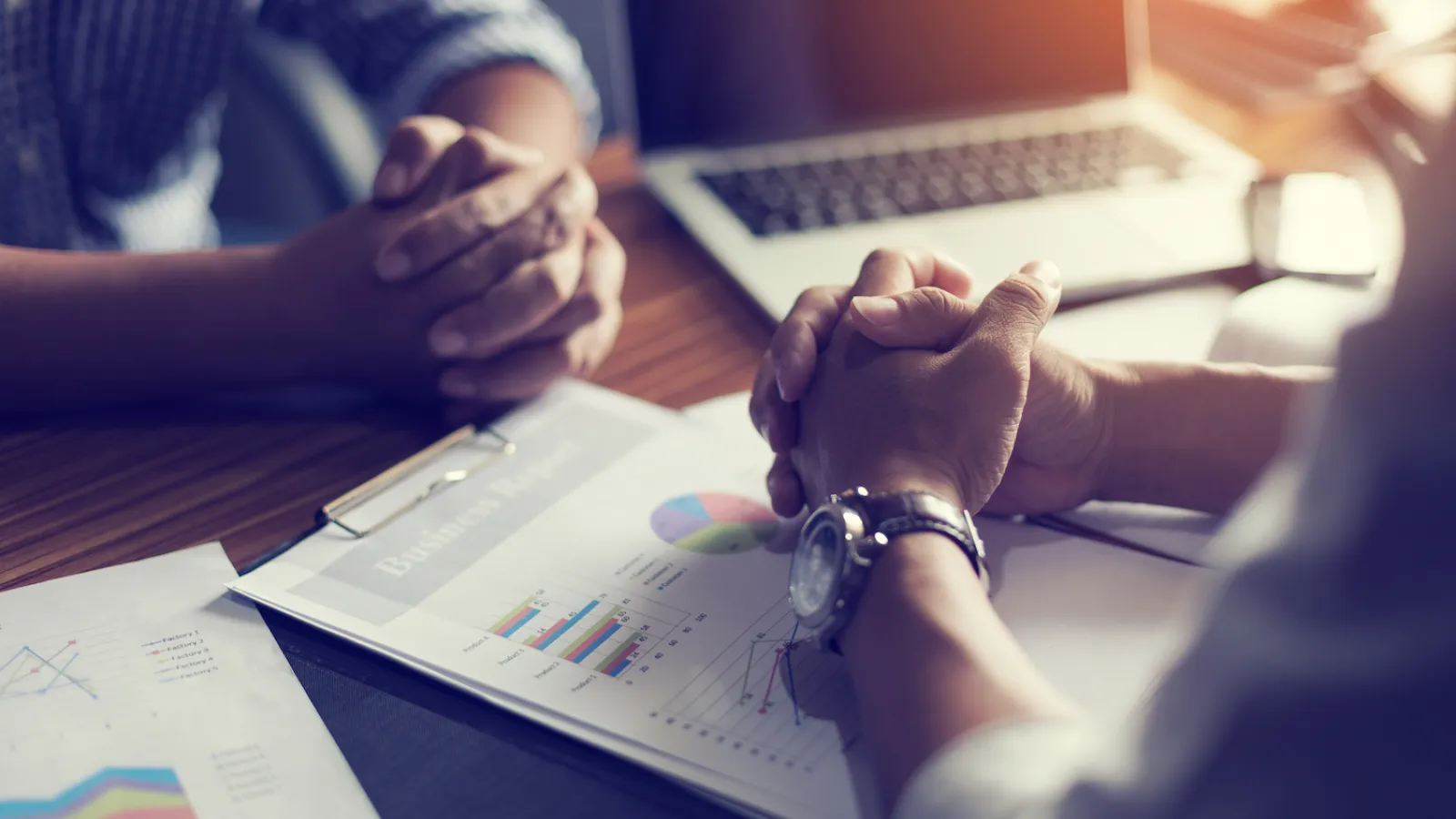 Two people discussing business charts and graphs with a laptop in a bright office setting.