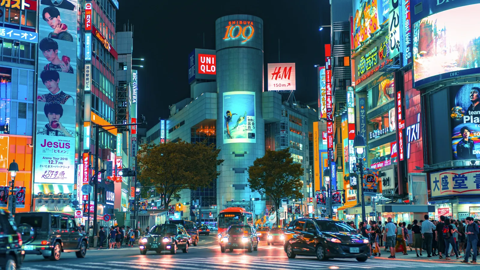 Nighttime view of Shibuya crossing Tokyo with illuminated billboards, cars, and pedestrians under bright city lights