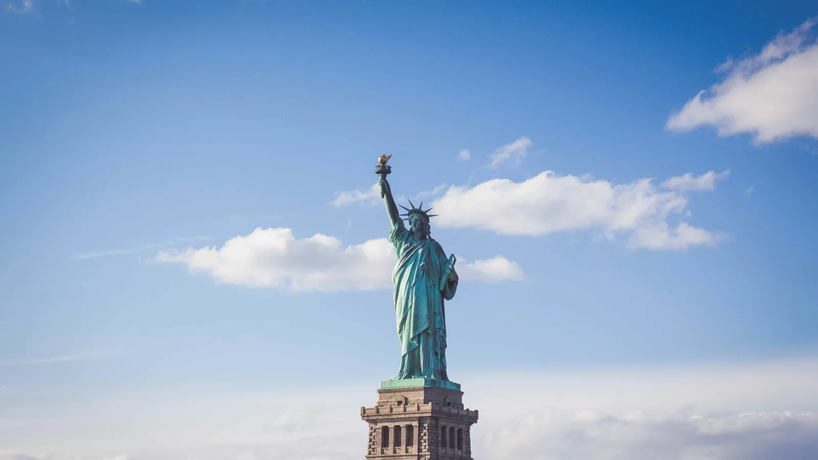 Statue of Liberty standing tall with a torch against a partly cloudy blue sky background.