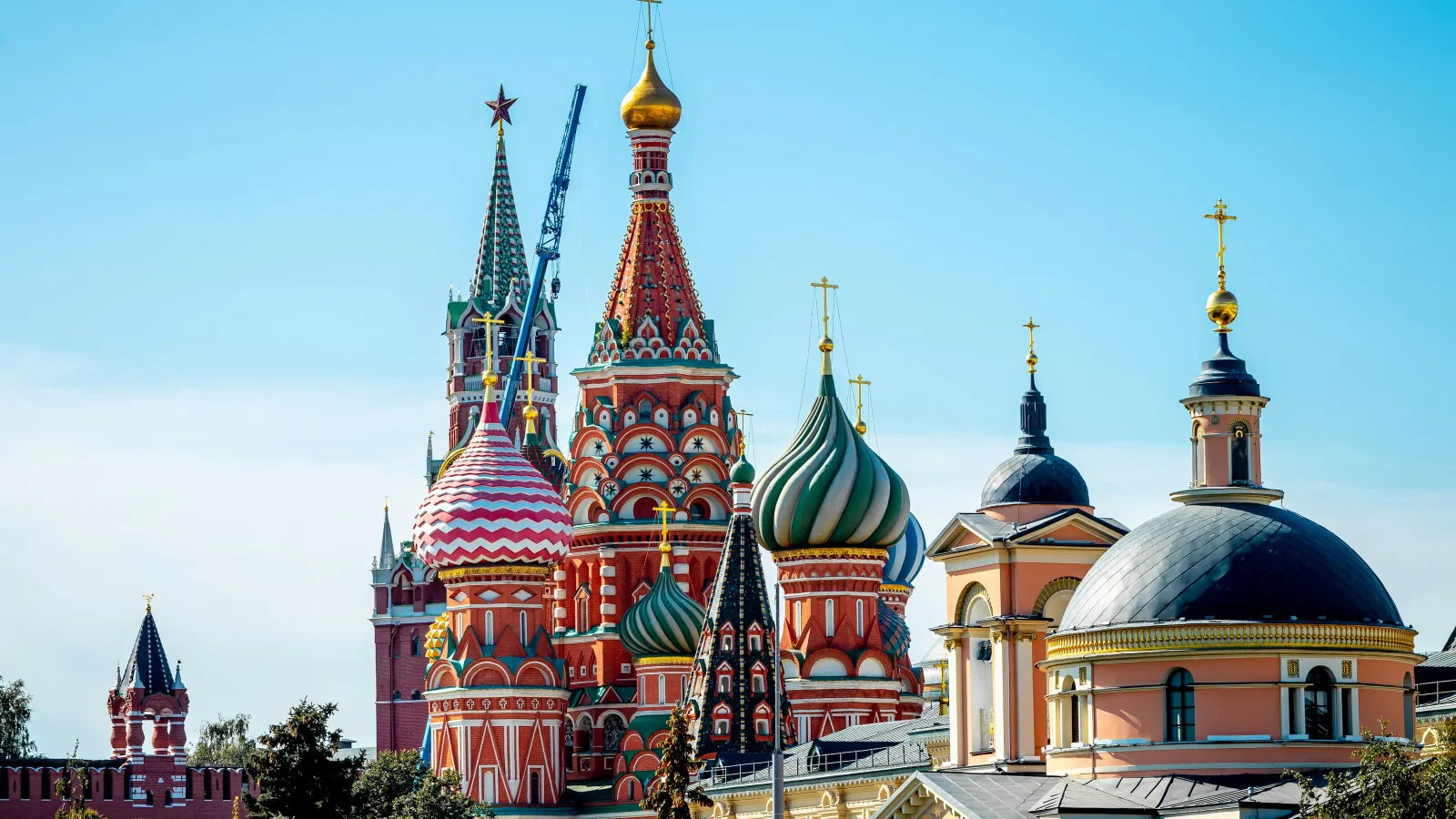 Colorful onion domes of Saint Basil's Cathedral in Moscow under a clear blue sky with surrounding historic buildings.