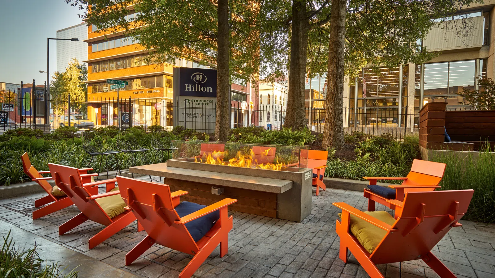 Outdoor seating area with orange chairs around a modern rectangular fire pit at Hilton hotel courtyard.