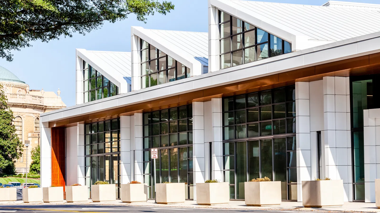 Modern building with slanted white roofs and large glass windows on a sunny day, surrounded by planters.