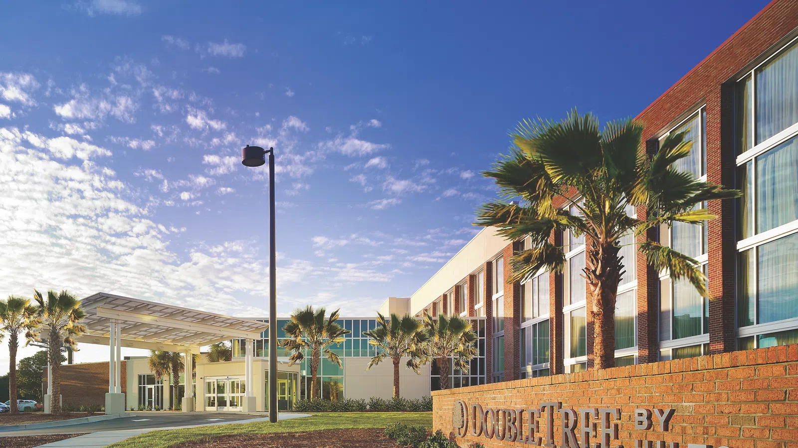 Exterior of DoubleTree by Hilton hotel with palm trees and a clear blue sky at sunset.