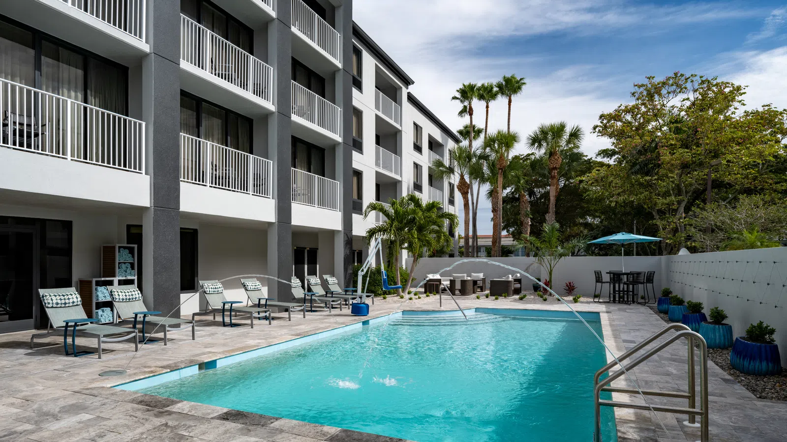 Modern apartment complex with a clean outdoor pool, lounge chairs, palm trees, and blue sky.
