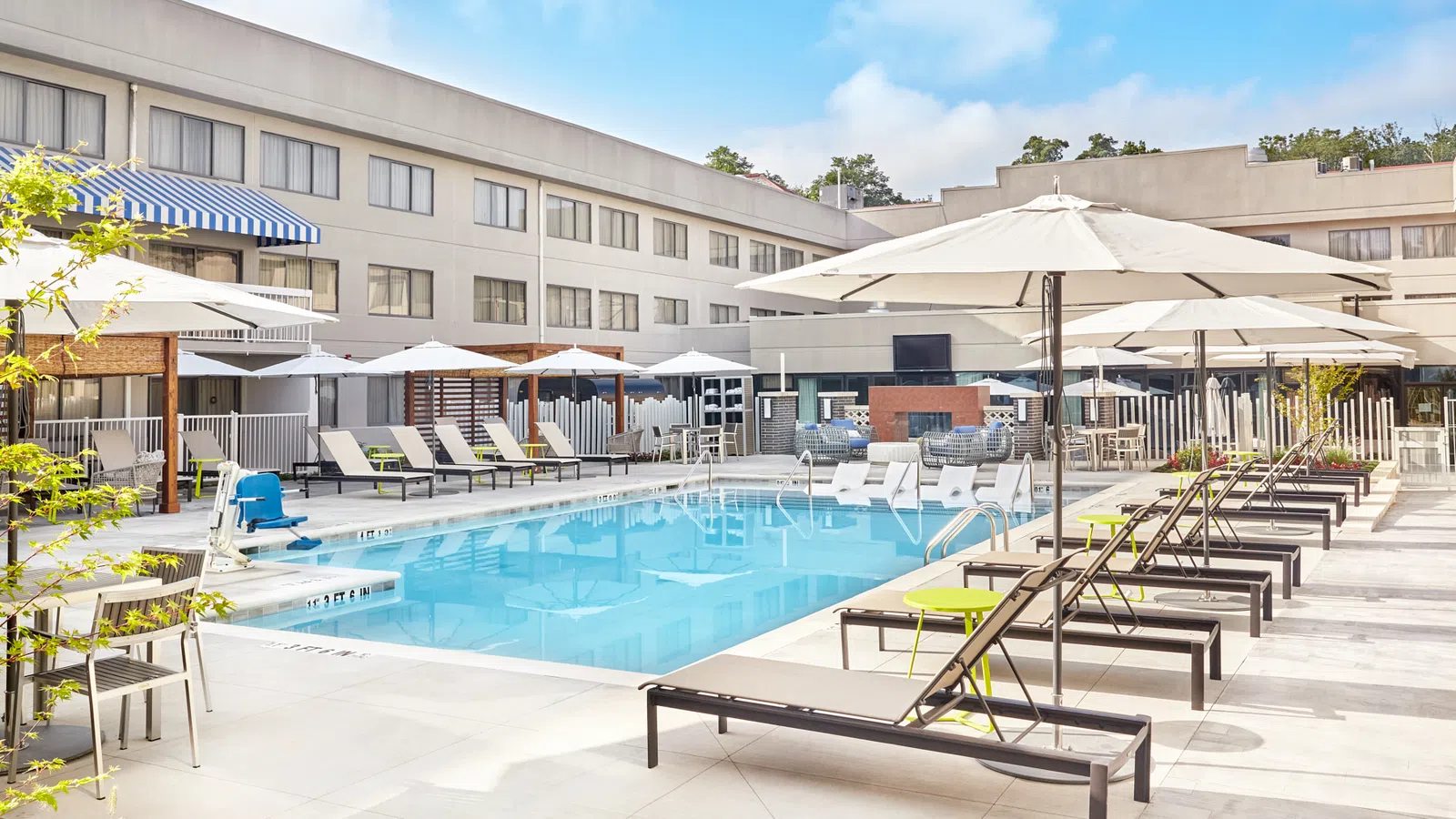 Outdoor hotel pool area with lounge chairs, white umbrellas, and clear blue water under a bright sky.
