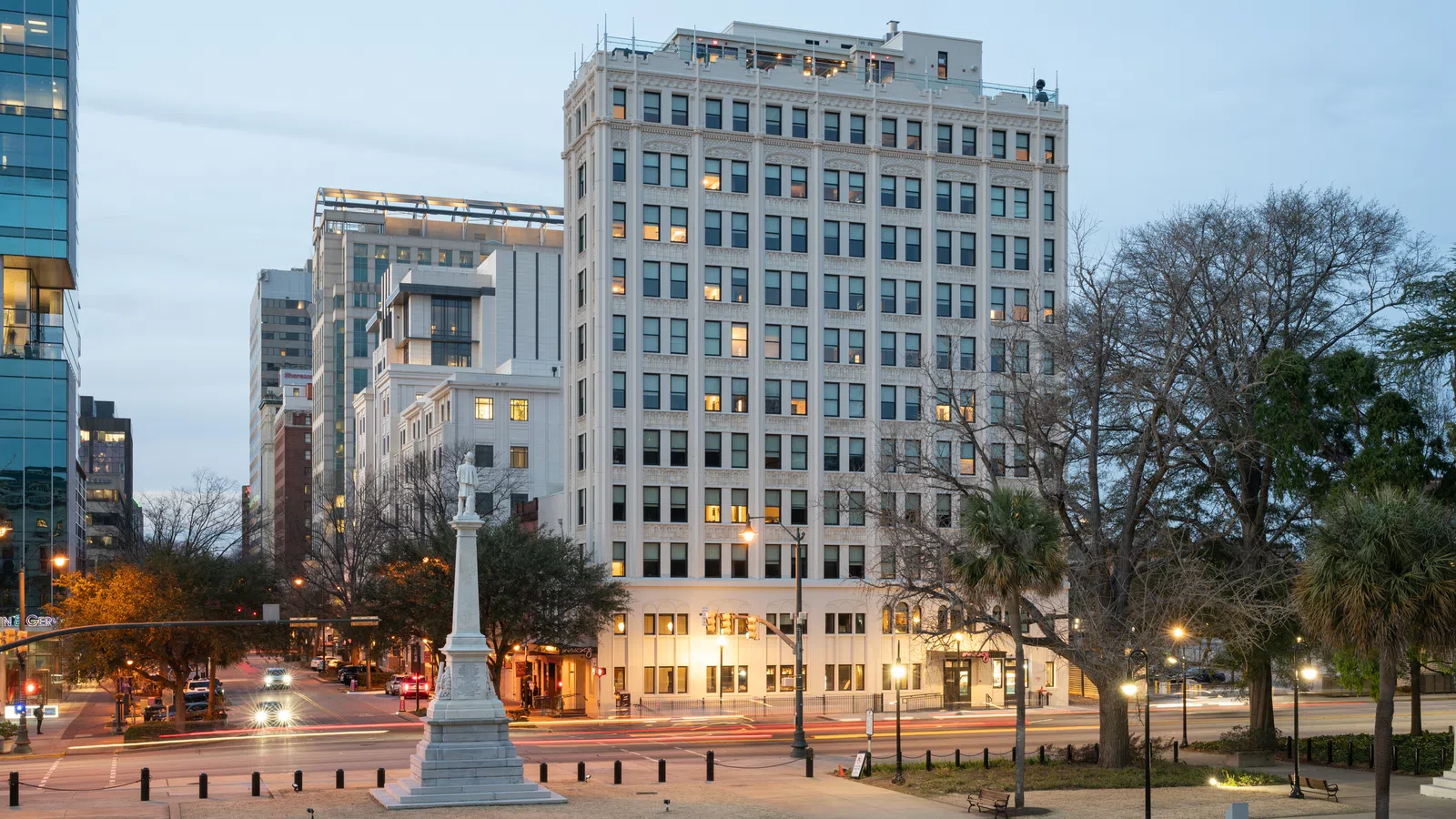 Downtown cityscape at dusk with historic monument, office buildings, and streetlights illuminating the scene