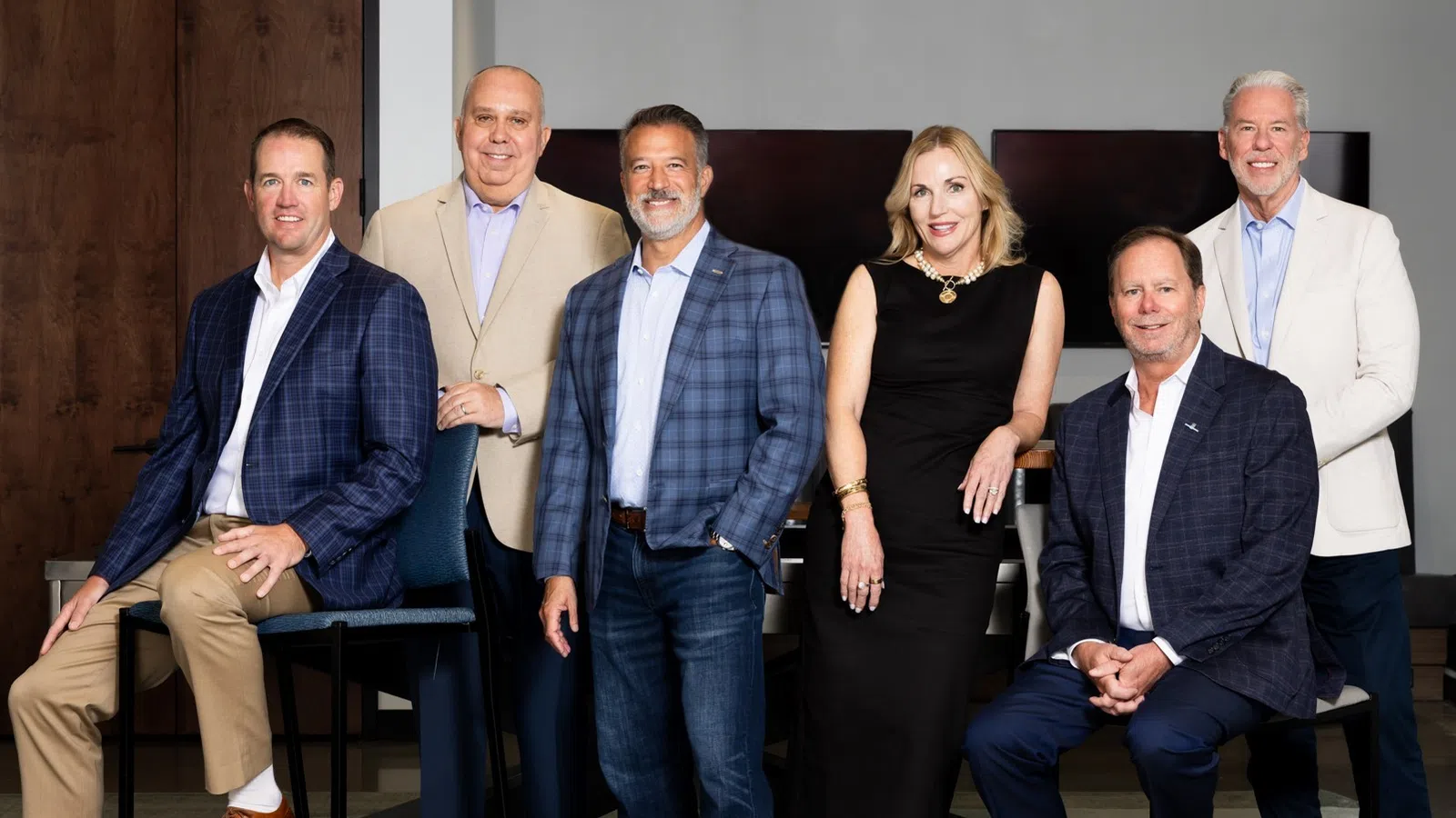 Group of six professionally dressed businesspeople posing in office setting with neutral background