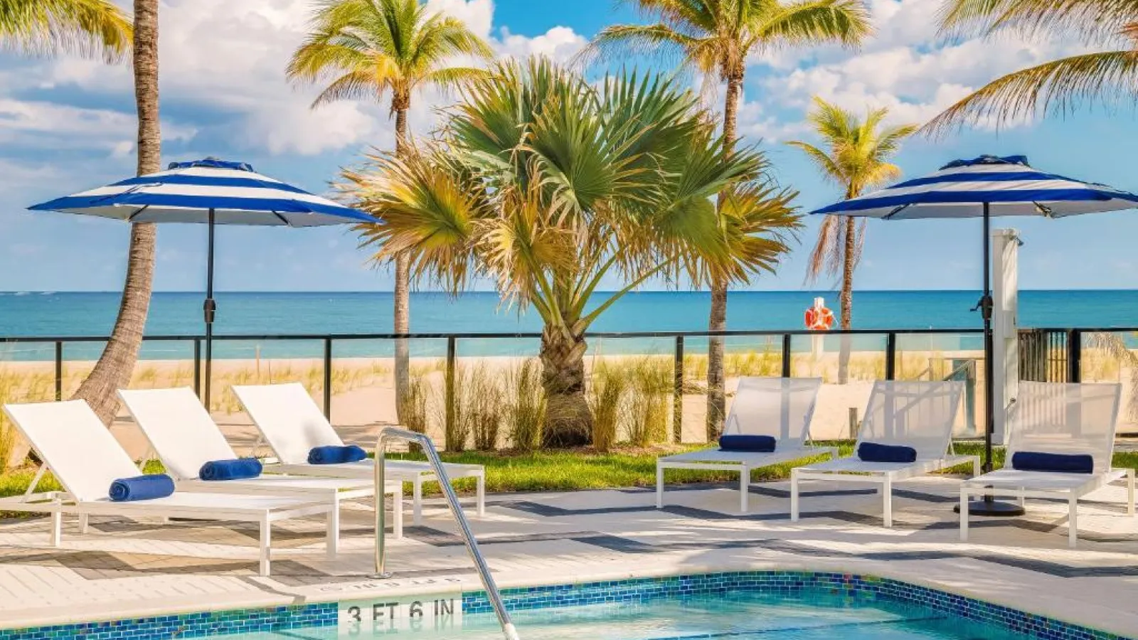 a pool with lounge chairs and umbrellas by a beach