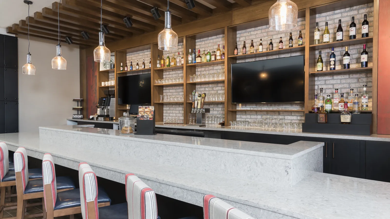 Modern bar interior with marble countertop, wooden shelves, hanging pendant lights, and stocked liquor bottles.