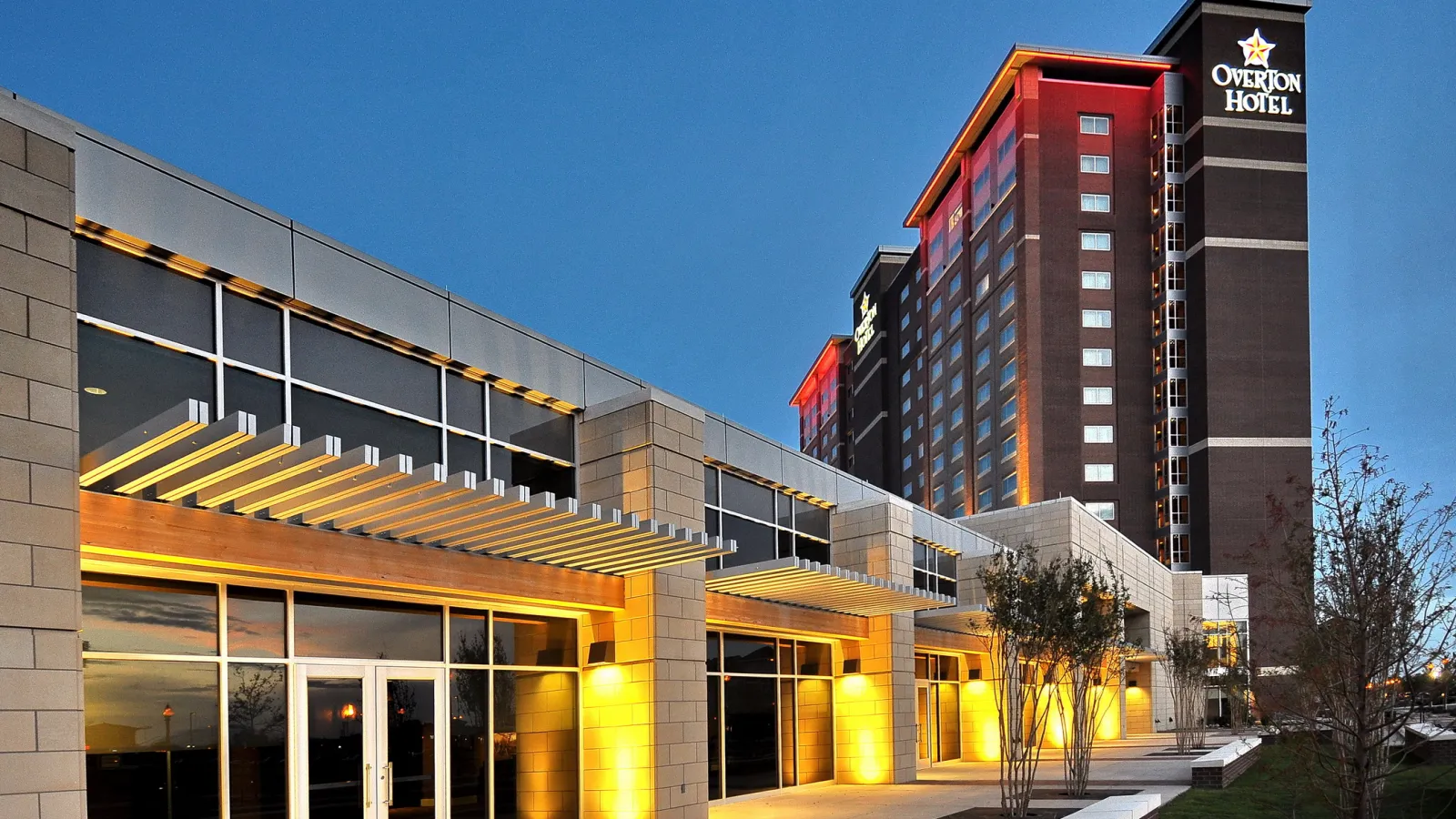 Modern Overton Hotel building exterior at dusk with illuminated entrance and tall tower under clear sky.