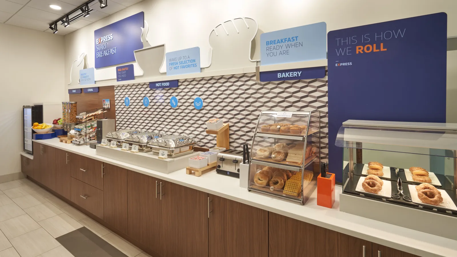 Hotel breakfast buffet with pastries, bagels, waffles, fruit, and hot food in a modern setup