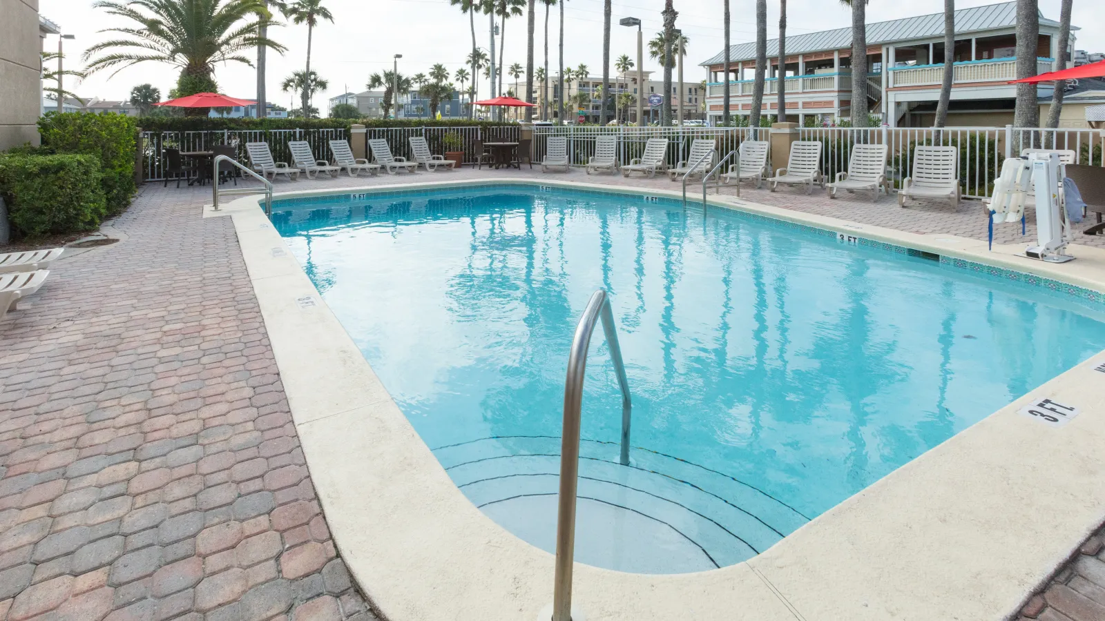 Outdoor swimming pool with lounge chairs and palm trees in a sunny, relaxed setting.