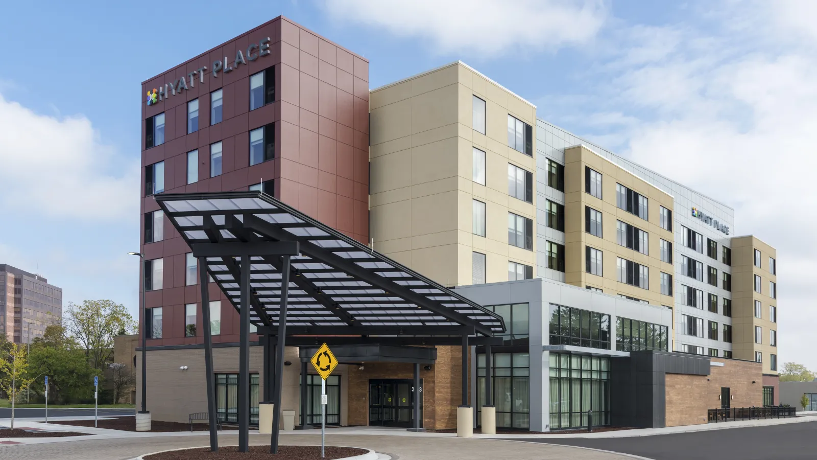 Modern Hyatt Place hotel building with glass entrance canopy under blue skies in urban area.