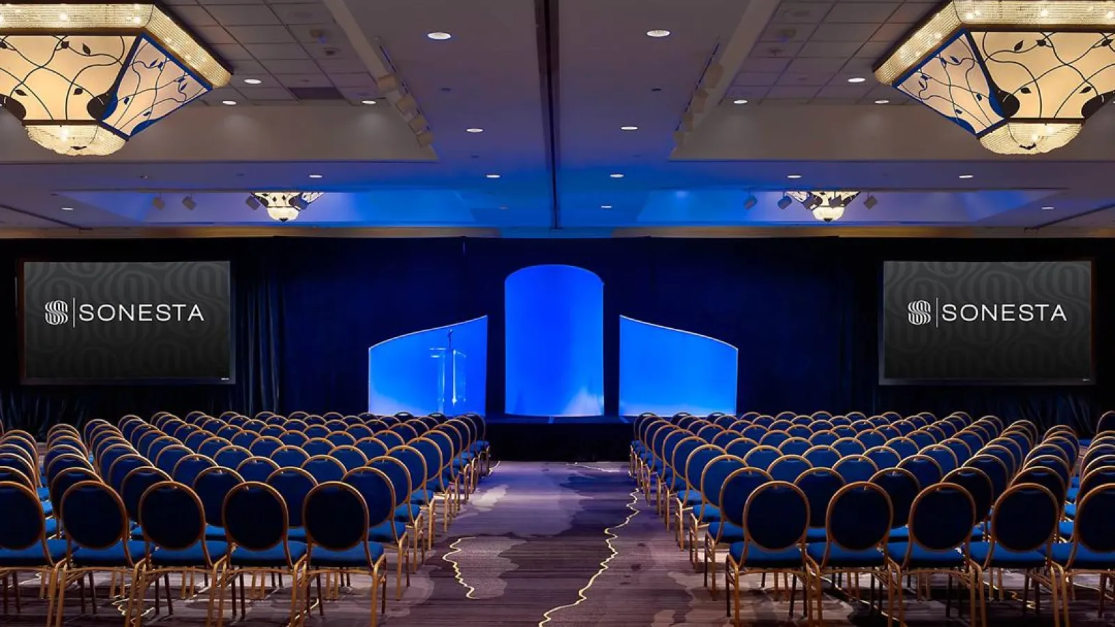 a room with blue chairs and a stage with a screen and lights