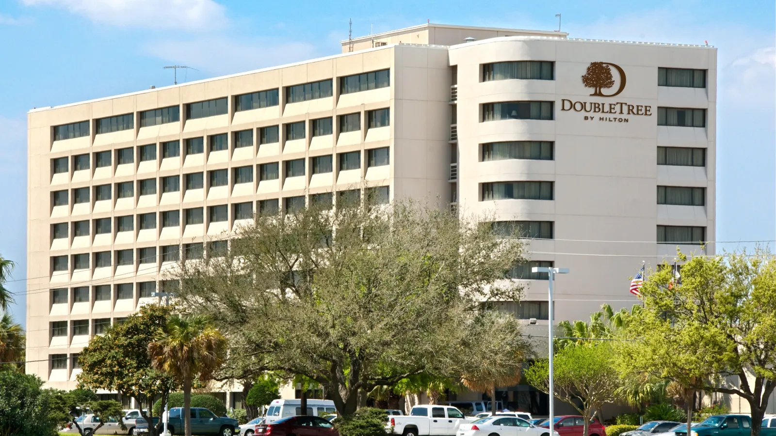 Exterior view of DoubleTree by Hilton hotel building with trees and parked cars under a blue sky.
