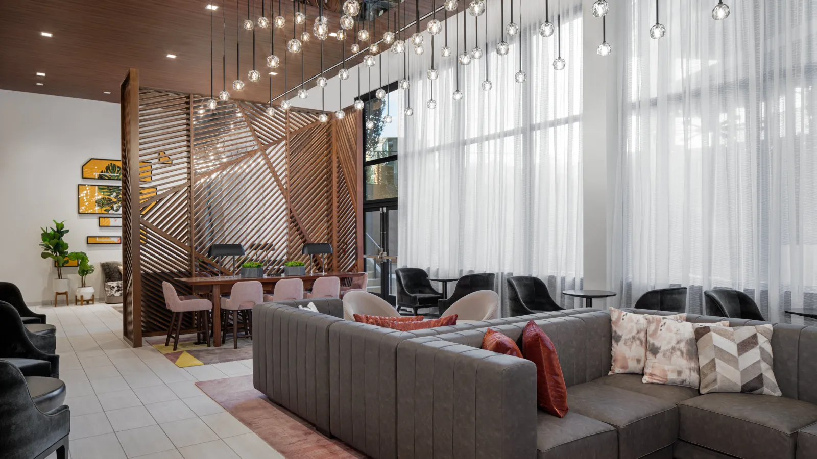 Modern lounge with gray sectional sofa, decorative pillows, hanging lights, and wooden partition in bright interior.