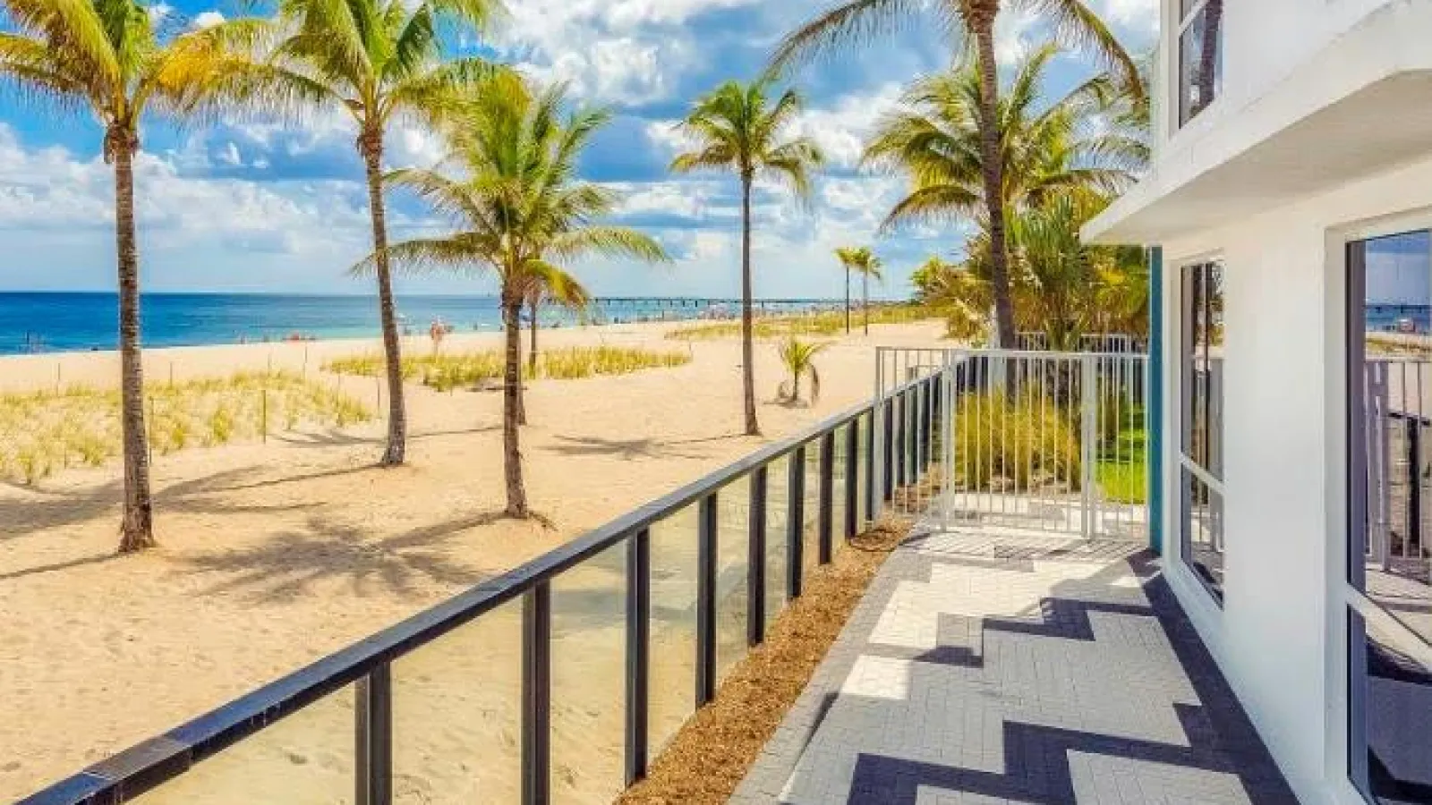 a walkway with palm trees and a body of water in the background