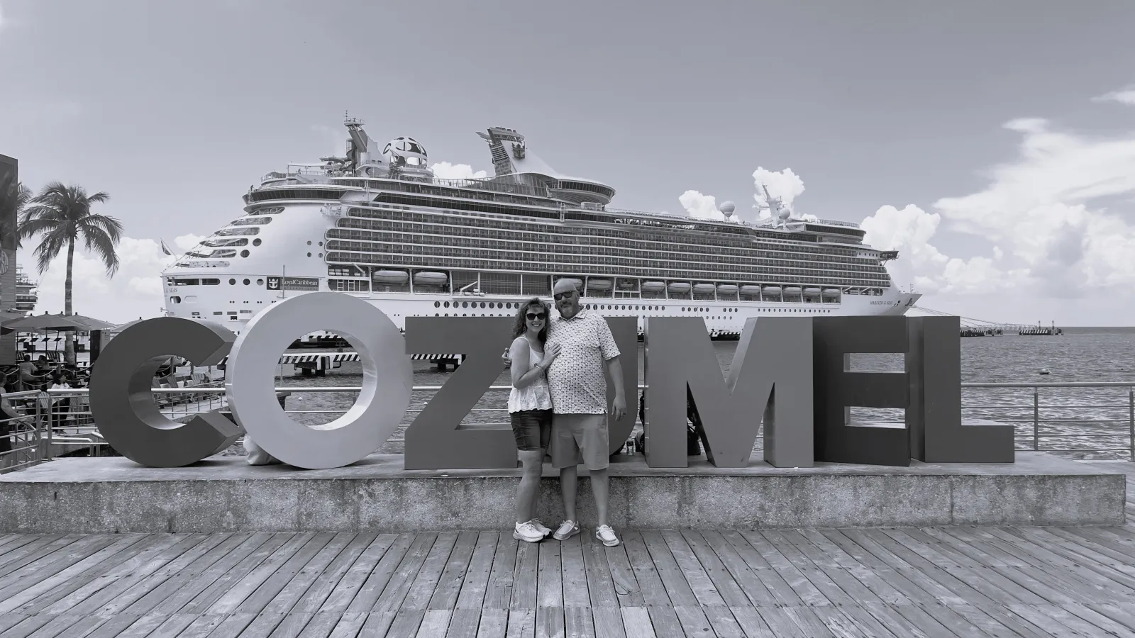 a man and woman posing in front of a large cruise ship