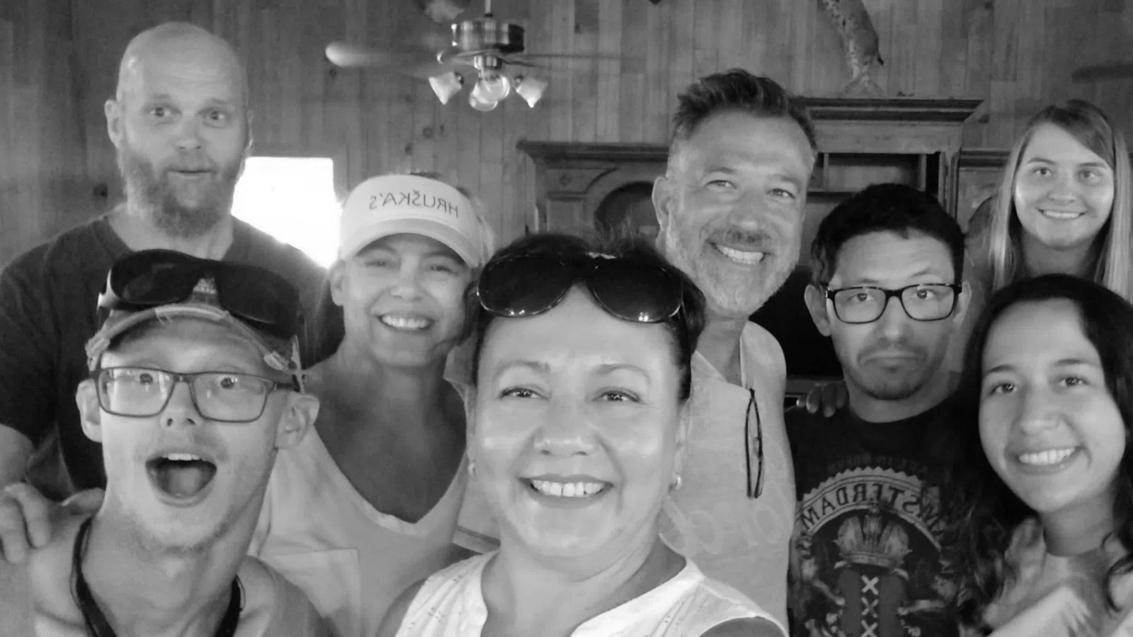 Group of nine diverse people smiling indoors in a cozy wooden room, taking a cheerful selfie together