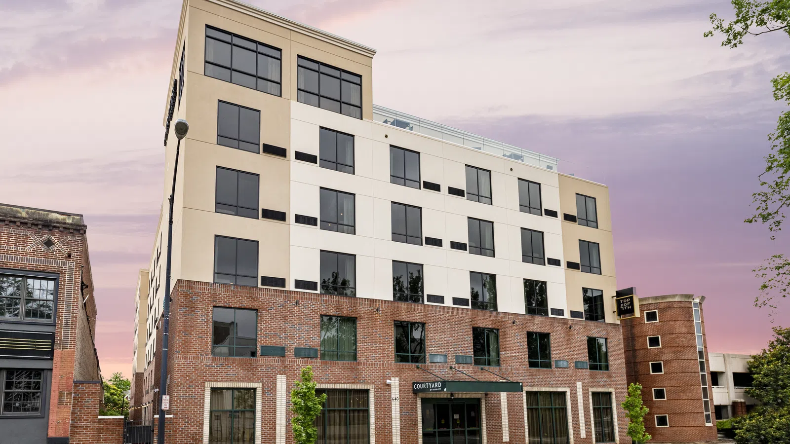 Modern mixed-use building with brick and beige facade under a pink and purple sunset sky.