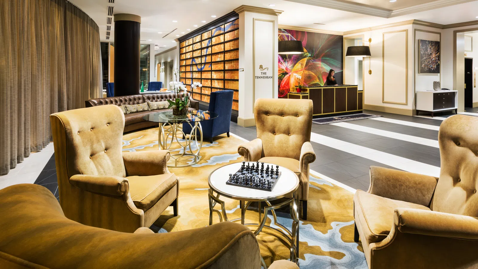 Luxury hotel lobby with plush chairs, chess set on table, modern artwork, and elegant lighting and decor.