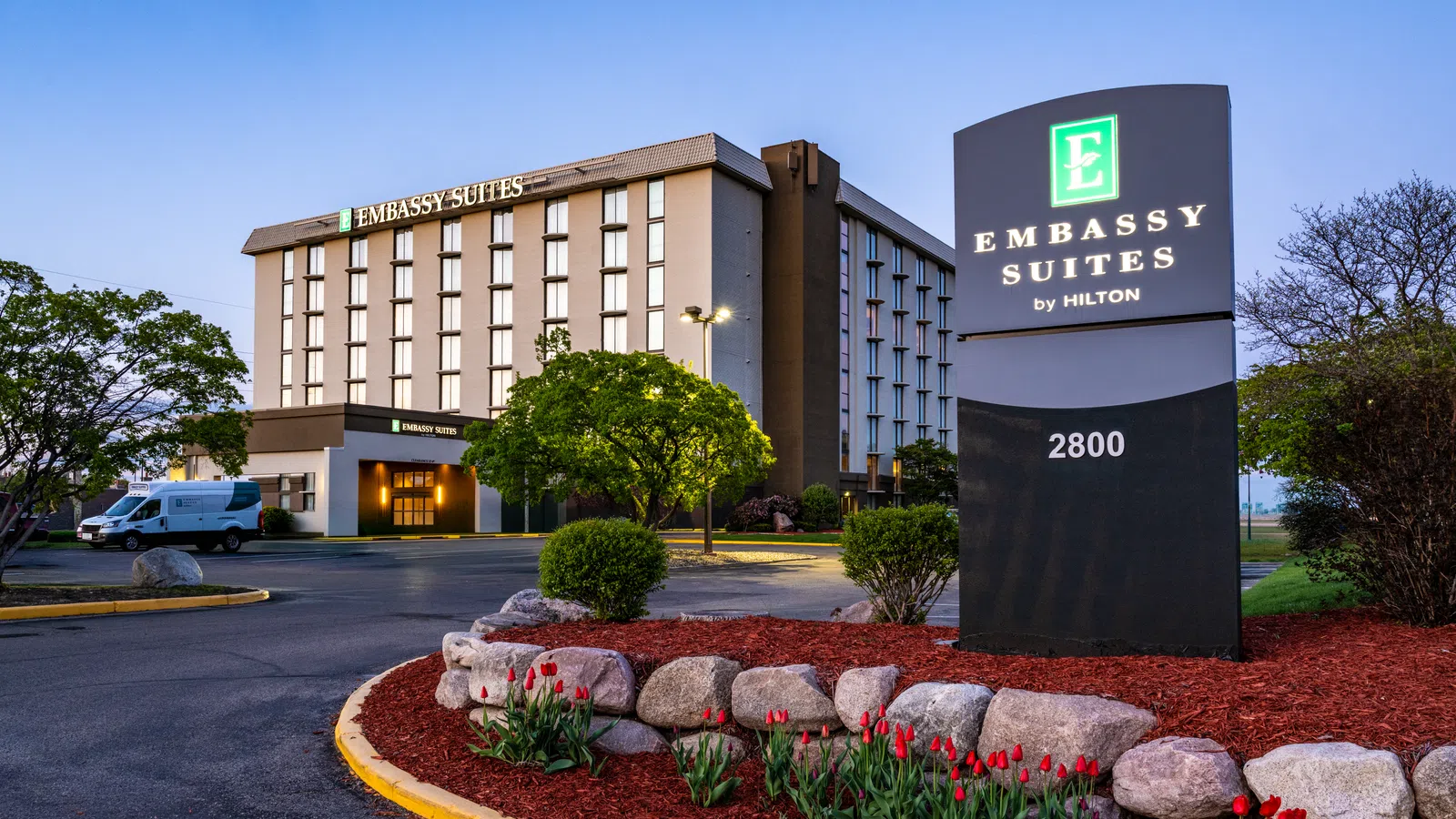 Embassy Suites by Hilton hotel exterior at dusk with landscaped entrance and illuminated signage.
