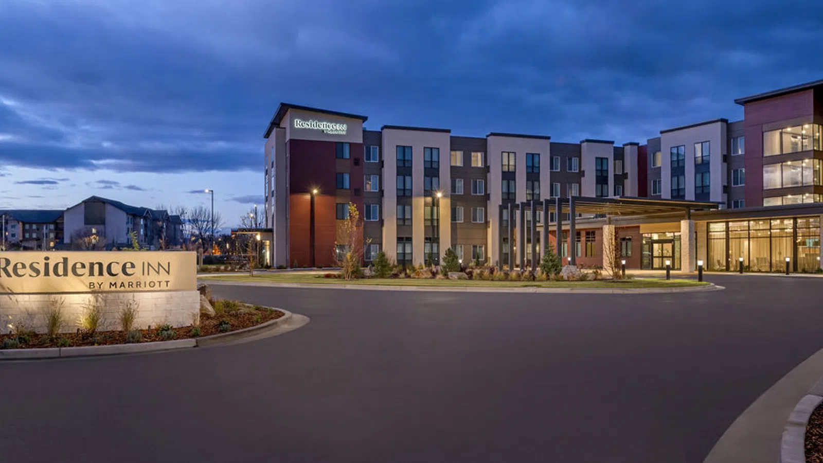 Residence Inn by Marriott hotel building with illuminated sign and entrance at dusk with cloudy sky.
