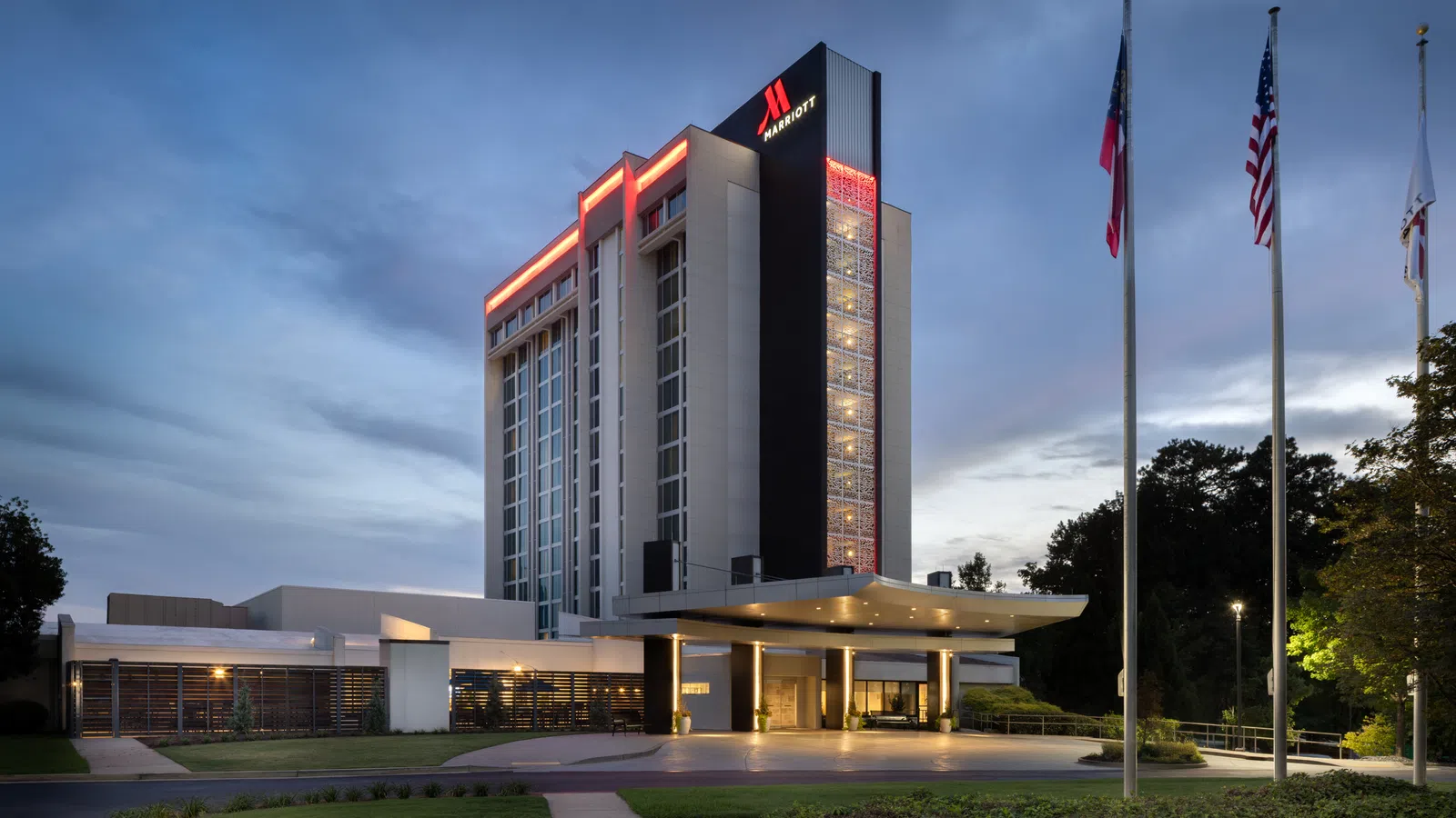 Marriott hotel building at dusk with illuminated signage and flags in front against a cloudy sky.