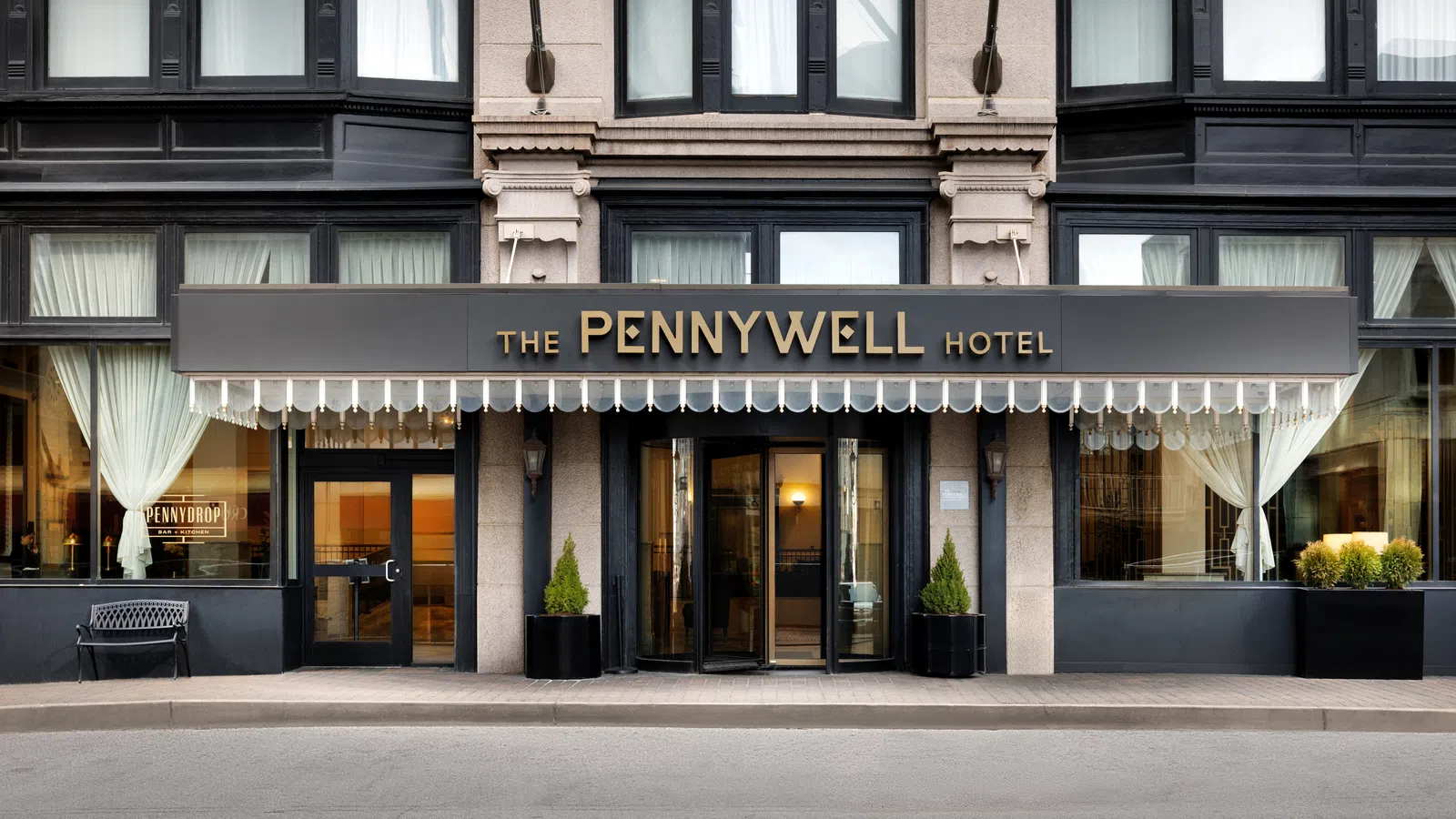 Entrance to The Pennywell Hotel with gold signage, large windows, and black decorative awning in an urban setting
