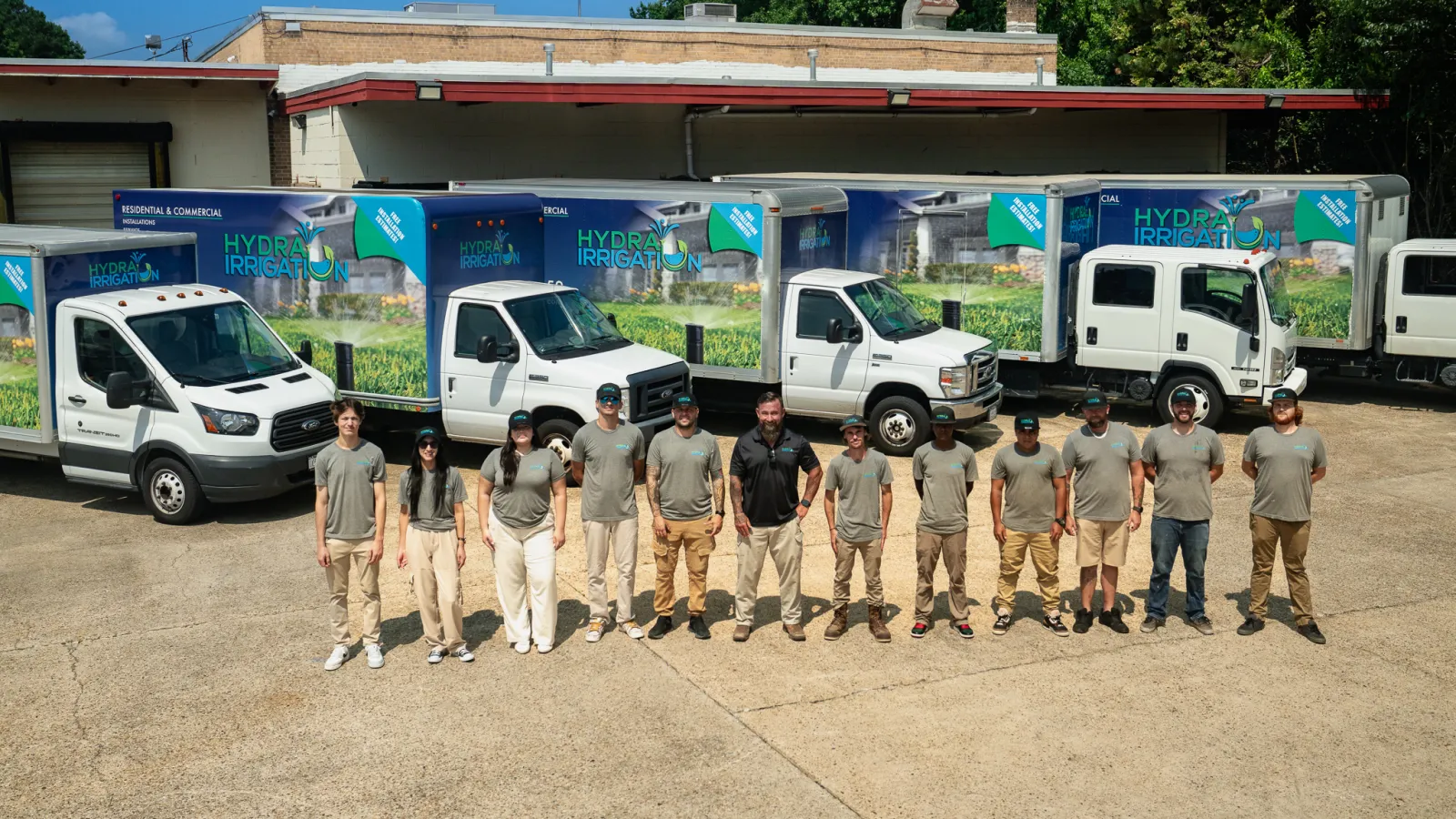 Hydra Irrigation team standing in front of branded company trucks with a clear sky and trees in the background