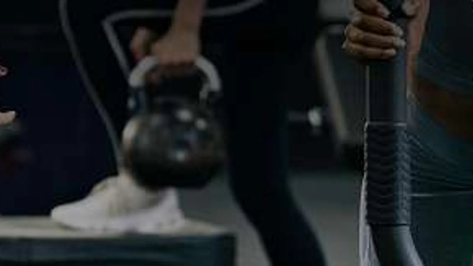 People exercising with kettlebells in a gym with dim lighting and fitness equipment.