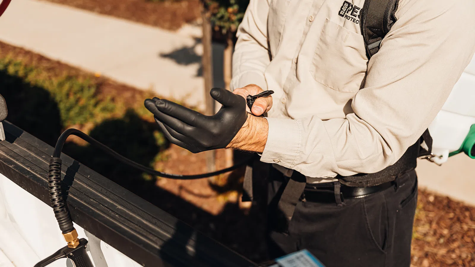 Pest control worker putting on black protective gloves next to equipment outdoors on a sunny day
