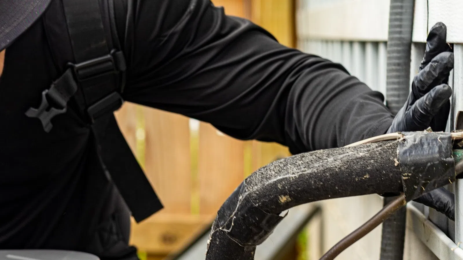 Technician in black clothes inspecting and repairing outdoor HVAC unit connections with gloved hands