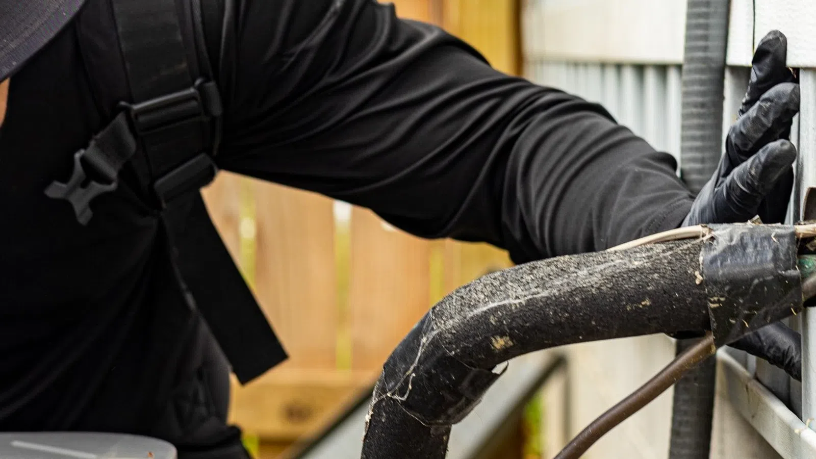 Technician in black clothes inspecting and repairing outdoor HVAC unit connections with gloved hands