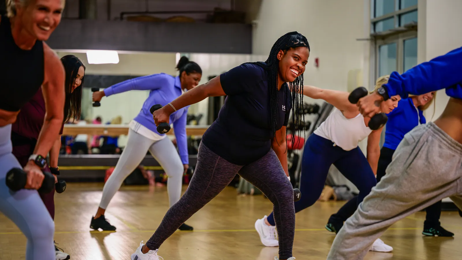 Group fitness class with diverse women lifting dumbbells and exercising in a gym studio