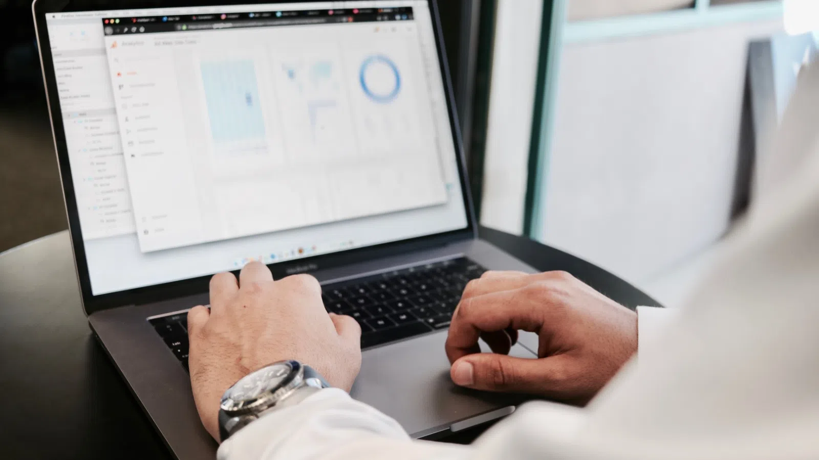 Person working on laptop displaying data charts and graphs on screen in a modern office setting