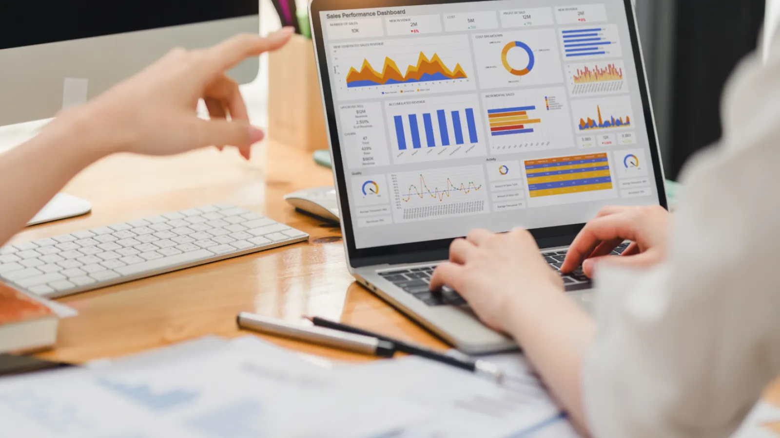 Two people analyzing sales performance charts and graphs on a laptop screen at a wooden desk.