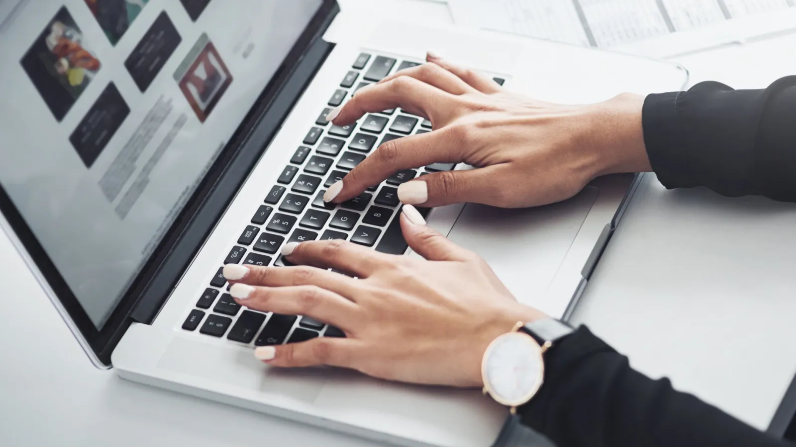 Person typing on a laptop keyboard with a website displayed on screen in a modern workspace.