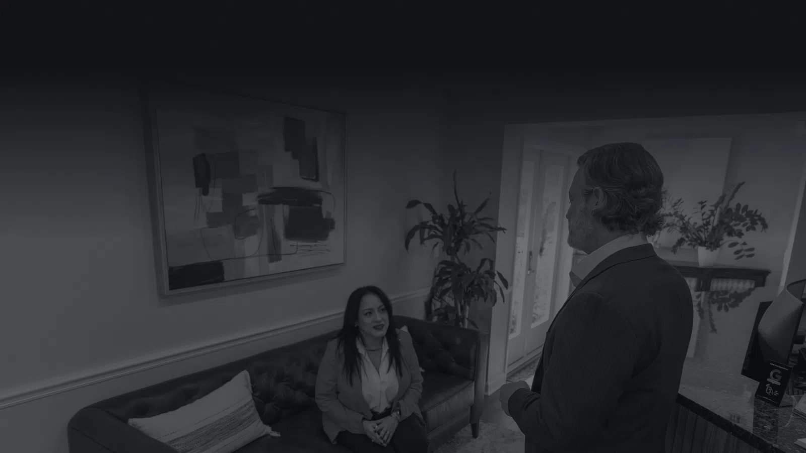Woman sitting on a couch talking to a standing man in a modern office with artwork and plants.