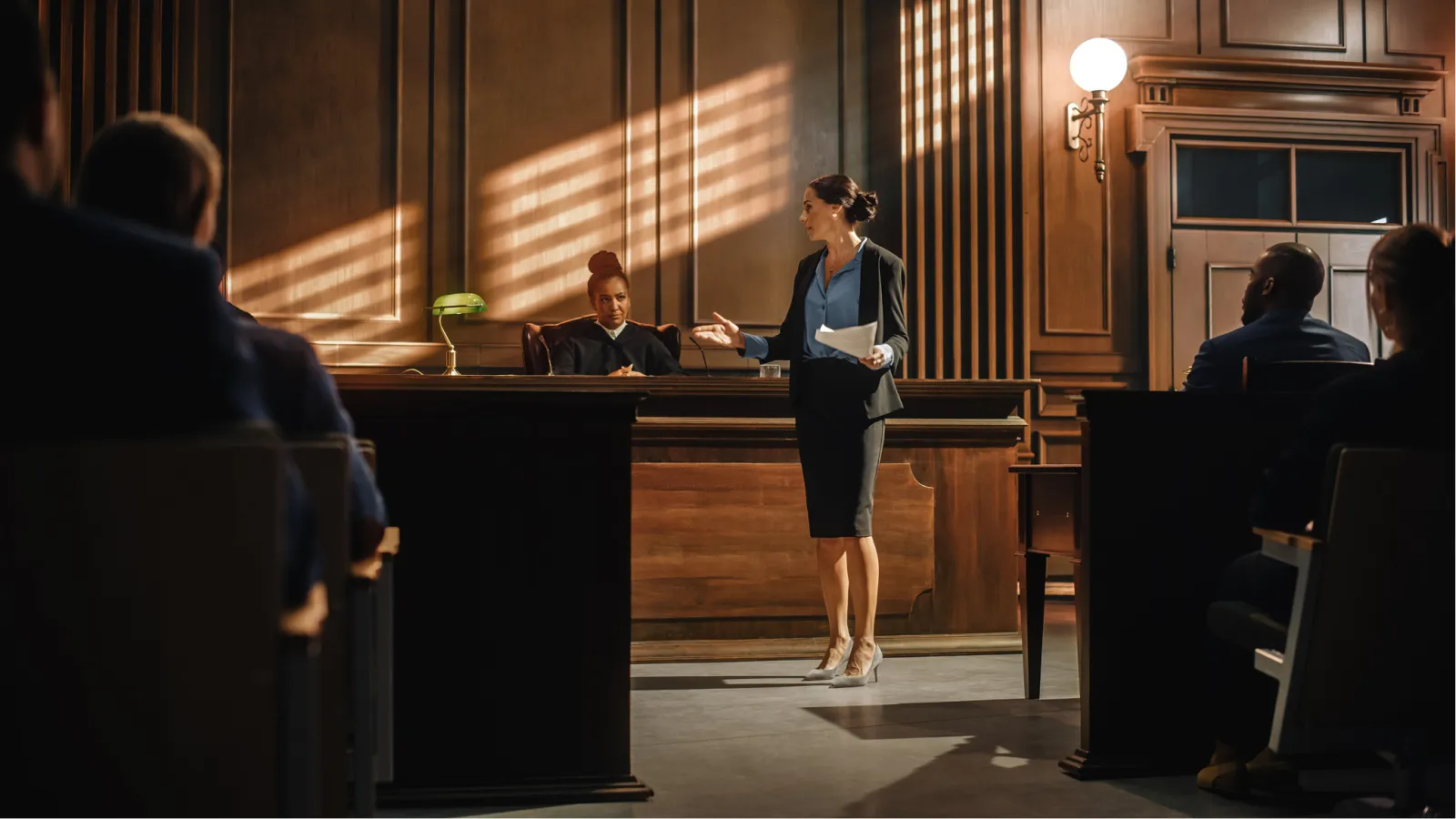 Woman lawyer presenting case to judge in a classic courtroom with audience and wooden wall panels