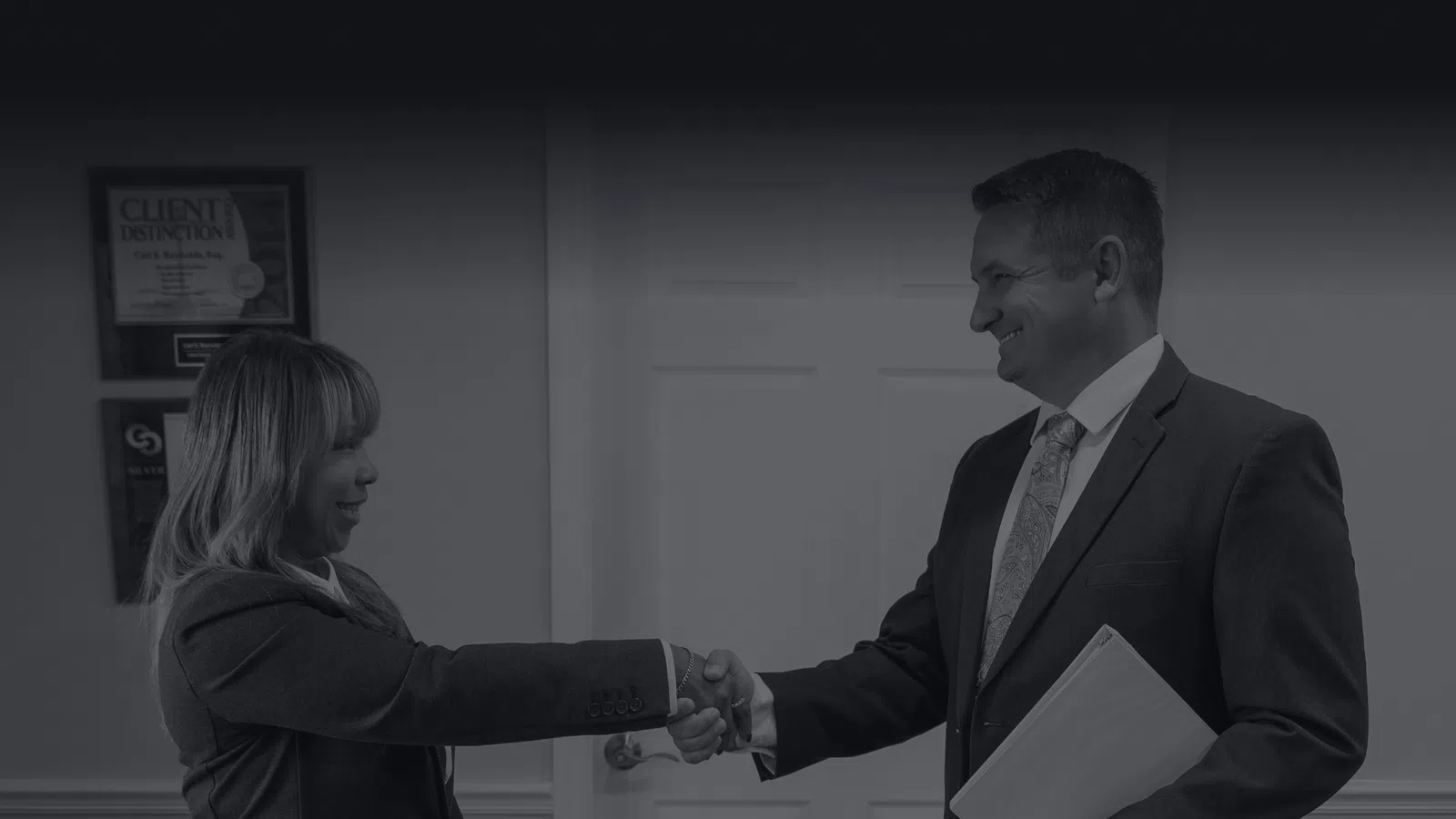 Two business professionals shaking hands in an office setting, symbolizing agreement and partnership.