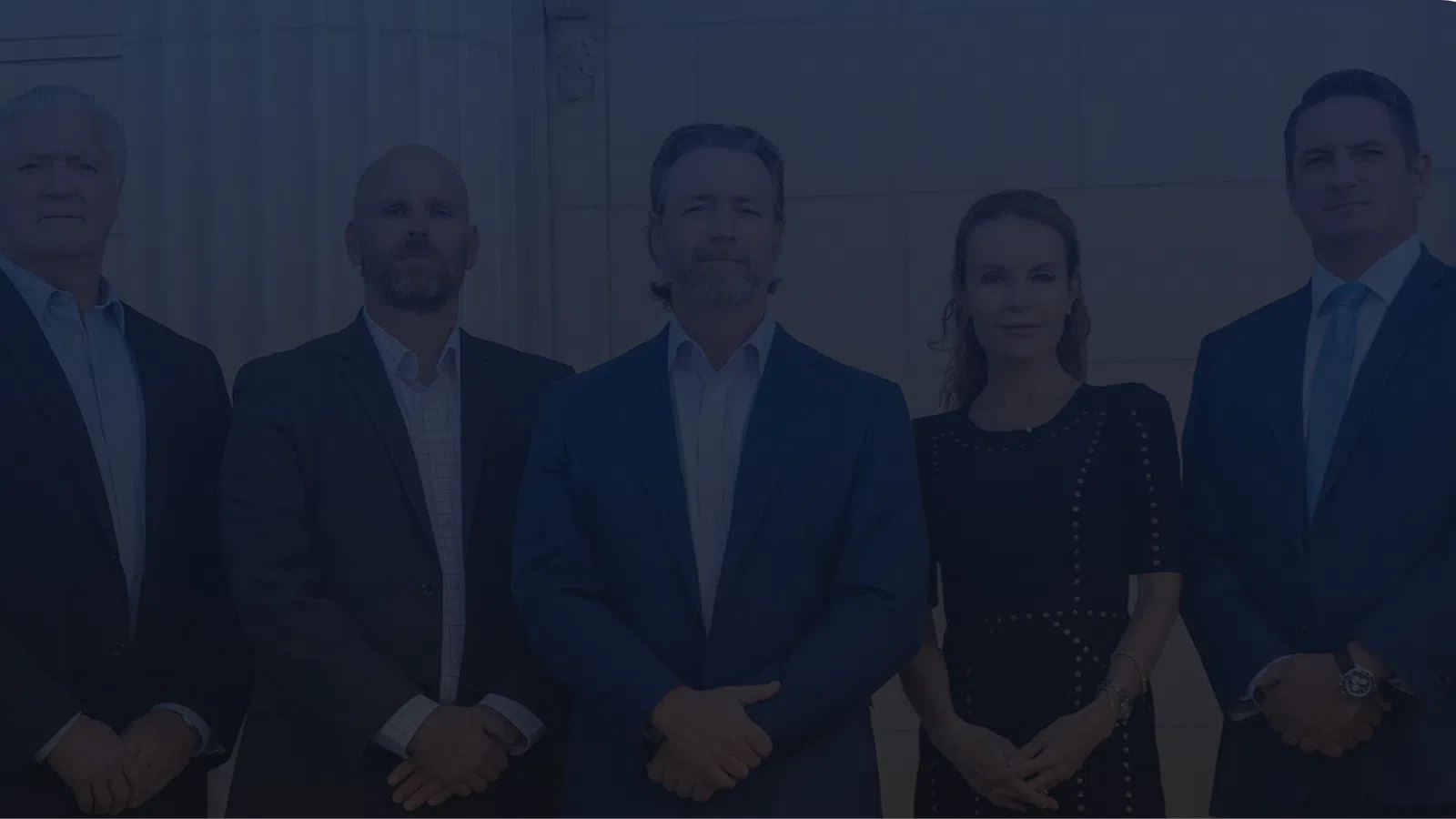Five business professionals standing in formal attire against a marble wall, posing confidently.