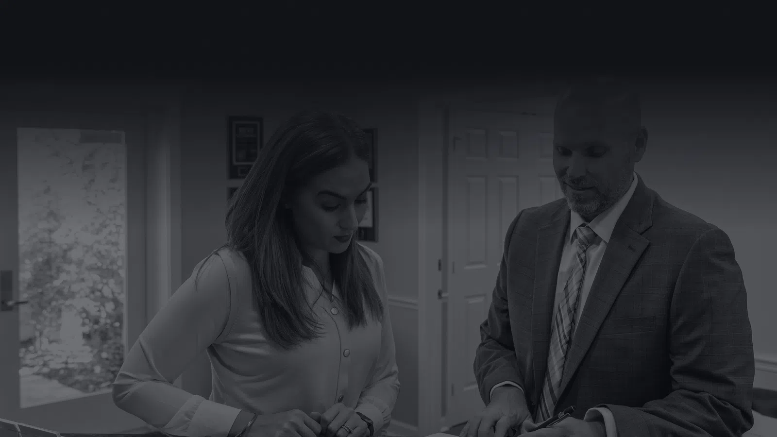 Man in suit explaining documents to woman at office reception desk in professional setting