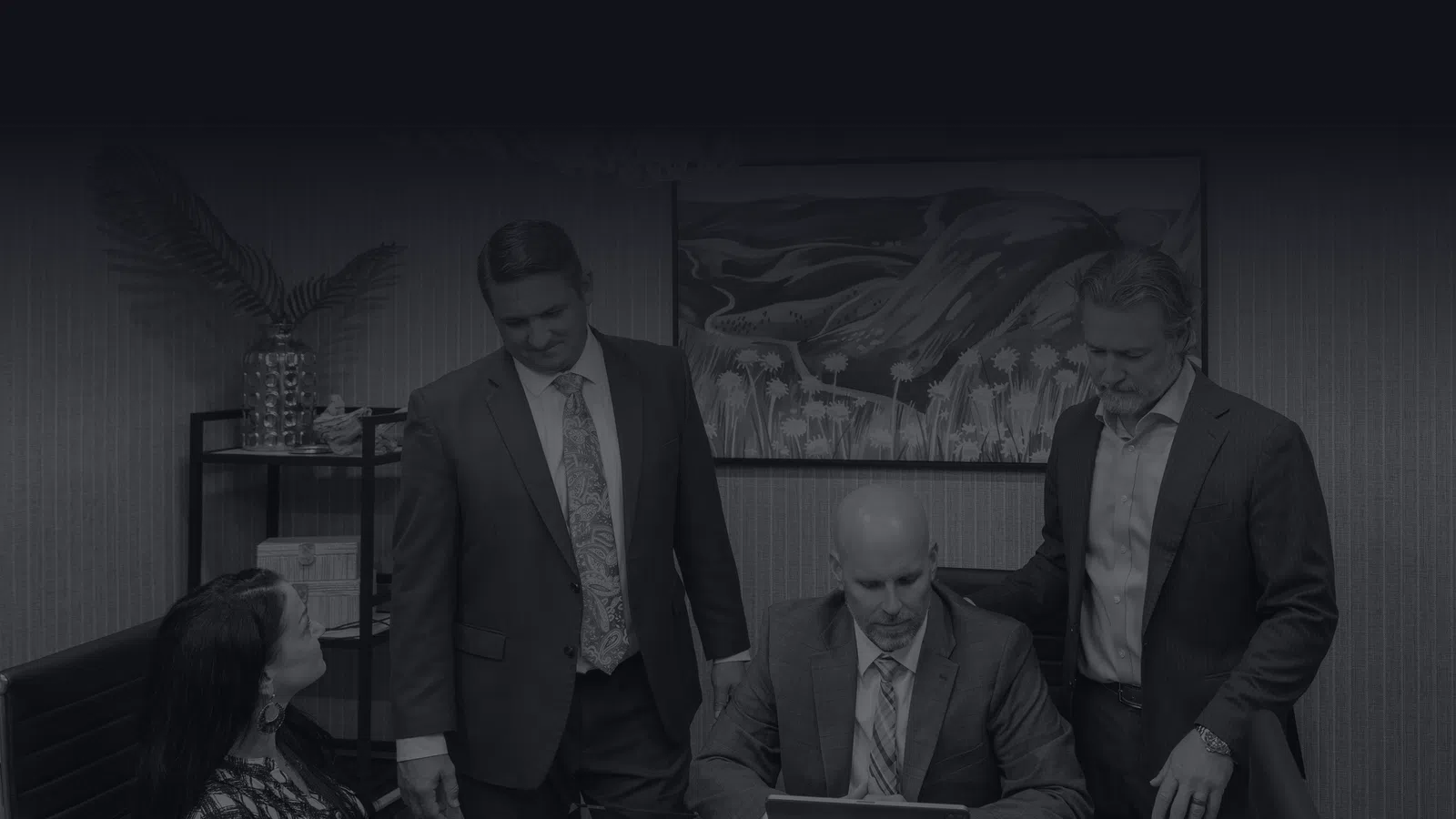 Four business professionals in suits collaborating around a glass table in a modern office setting.