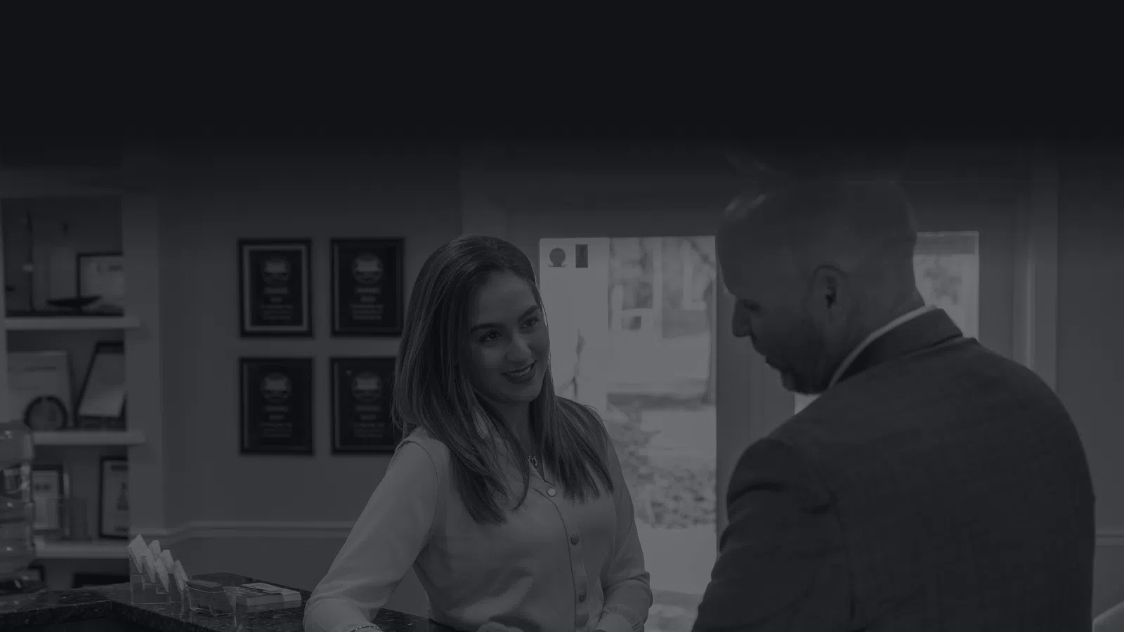 Receptionist handing a card to a man in a suit at a welcoming office front desk.