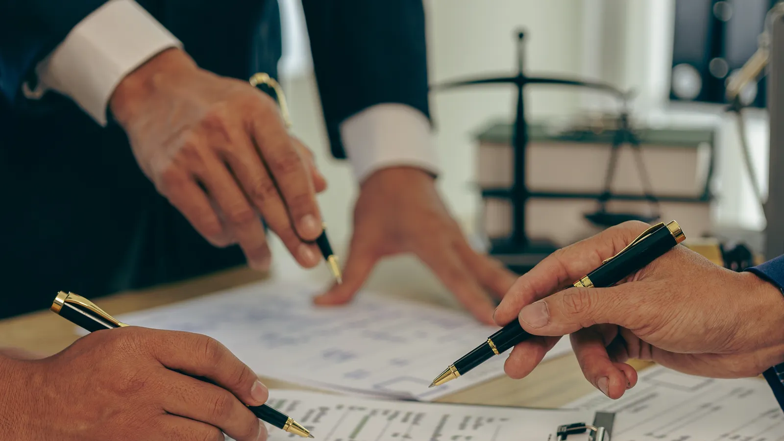 Business professionals reviewing and signing contracts on a wooden table with legal documents and pens.