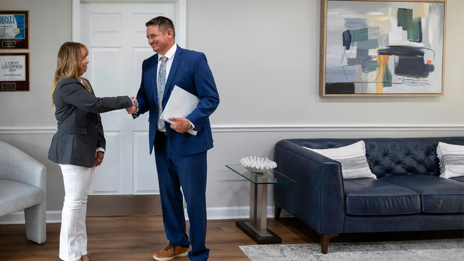 Senior man shaking hands with a younger man while a senior woman looks on in a bright office setting